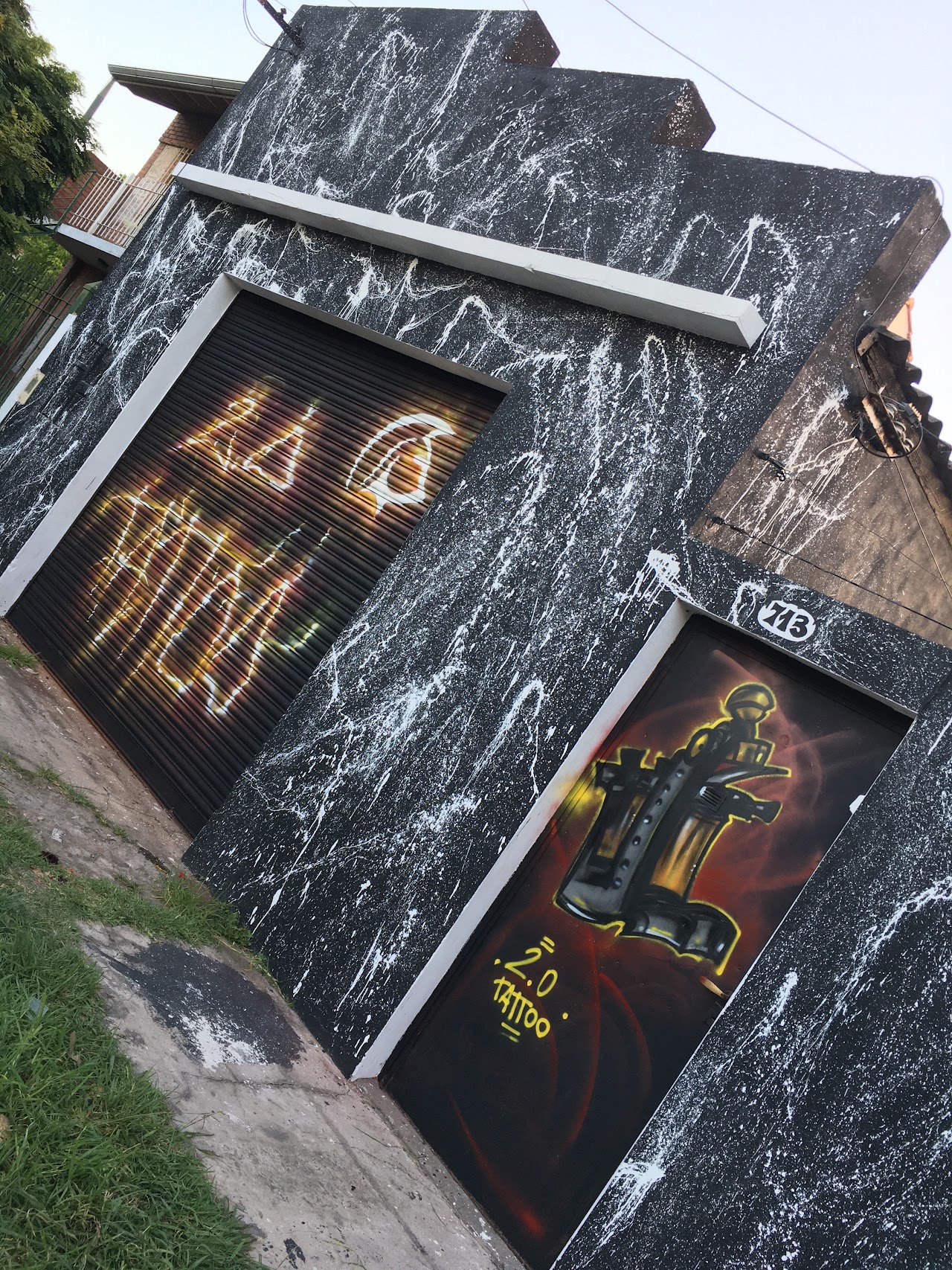 Fachada nocturna de 2.0 Tattoo con mural artístico de filigranas doradas, marquesina iluminada e interior vidriado estilo atelier en Berazategui